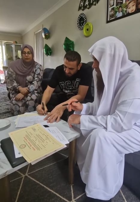 A bride and groom signing their marriage paperwork at home
